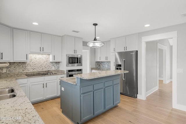 kitchen with appliances with stainless steel finishes, decorative light fixtures, white cabinetry, and a kitchen island with sink