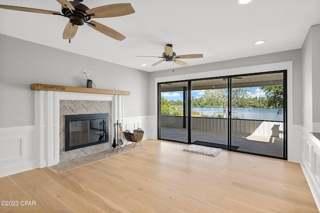 unfurnished living room featuring a tiled fireplace, a water view, a healthy amount of sunlight, and light wood-type flooring