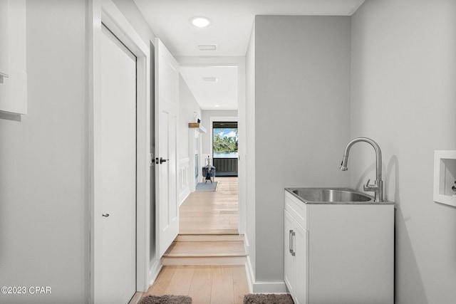 clothes washing area featuring cabinets, light wood-type flooring, and sink