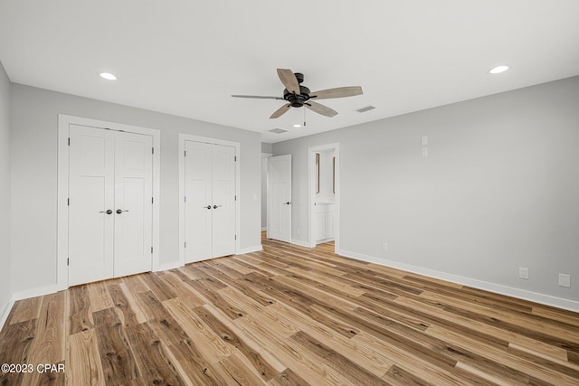 unfurnished bedroom featuring two closets, light hardwood / wood-style floors, and ceiling fan