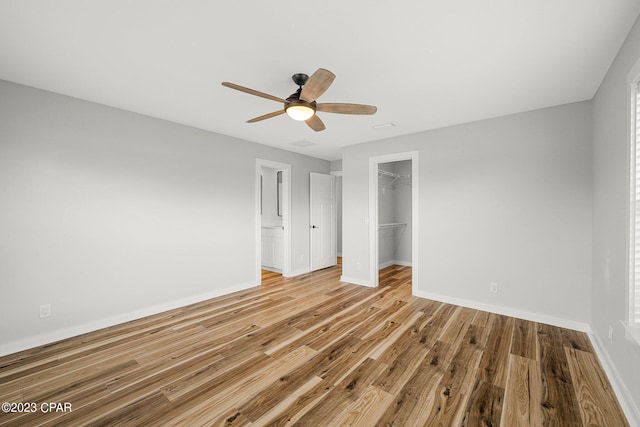 unfurnished bedroom featuring a spacious closet, a closet, ceiling fan, and light hardwood / wood-style floors