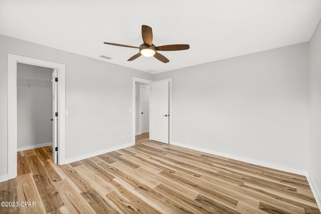 unfurnished bedroom featuring light wood-type flooring, a walk in closet, a closet, and ceiling fan