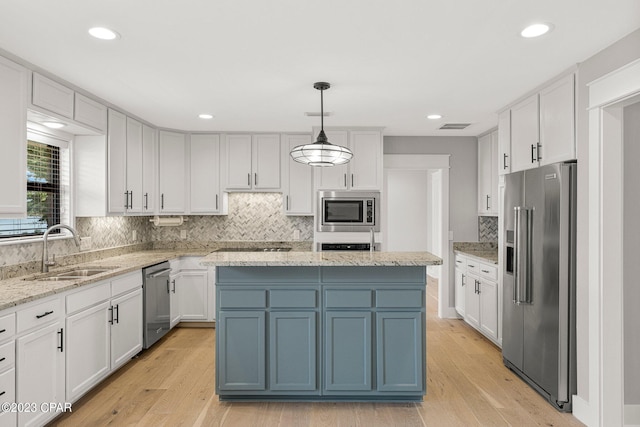 kitchen with a center island, sink, hanging light fixtures, white cabinets, and appliances with stainless steel finishes