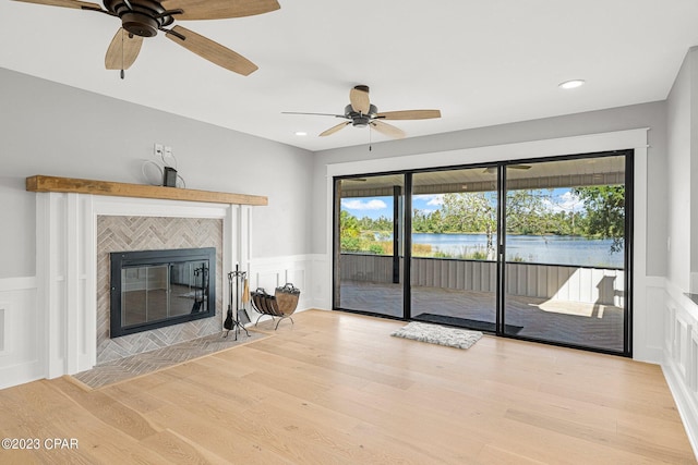 unfurnished living room featuring a tile fireplace, ceiling fan, a water view, and light hardwood / wood-style floors