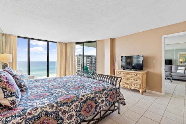 bedroom with light tile patterned floors, a water view, a textured ceiling, access to outside, and baseboards