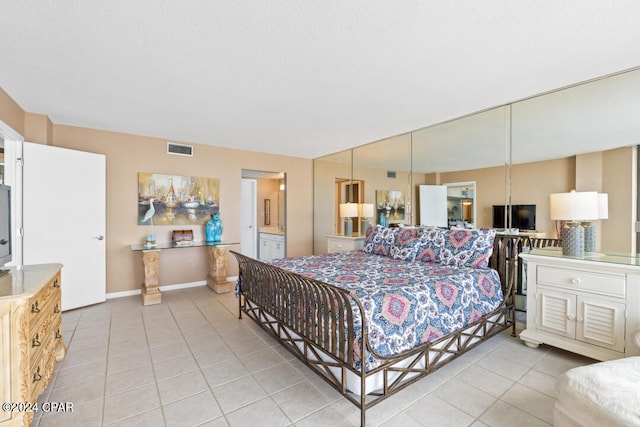 bedroom with ensuite bath, light tile patterned floors, baseboards, and visible vents