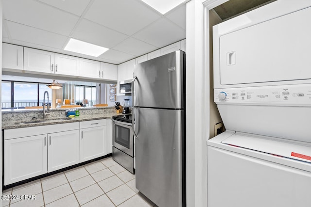 kitchen featuring light tile patterned floors, appliances with stainless steel finishes, stacked washing maching and dryer, white cabinetry, and a sink