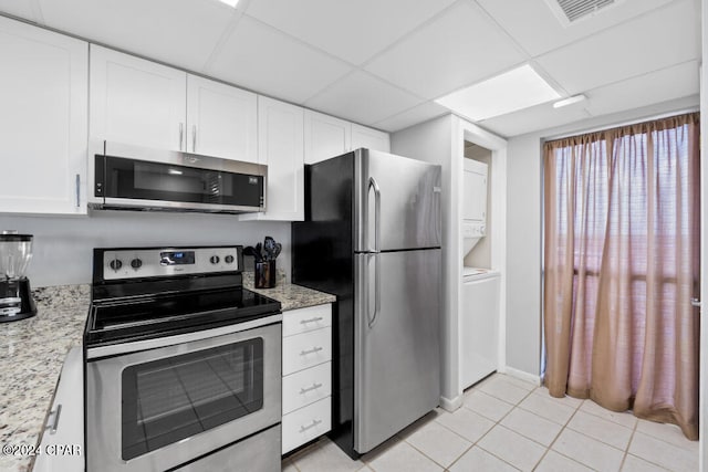 kitchen featuring light tile patterned floors, stainless steel appliances, white cabinetry, visible vents, and stacked washer / drying machine