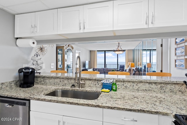 kitchen featuring white cabinets, a sink, stainless steel dishwasher, and light stone countertops