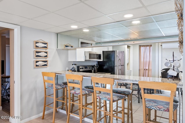 kitchen featuring stainless steel appliances, a drop ceiling, light tile patterned flooring, and white cabinets