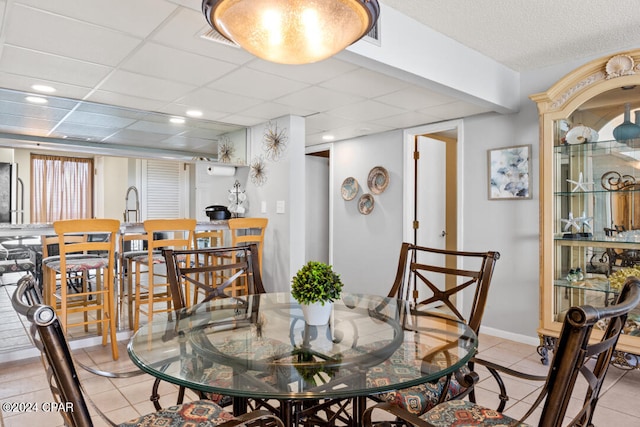 dining area featuring a paneled ceiling, baseboards, and light tile patterned floors