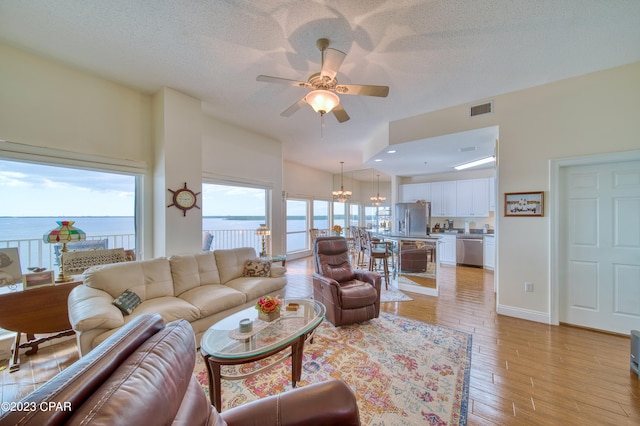 living room with ceiling fan with notable chandelier, light hardwood / wood-style floors, a water view, and a textured ceiling