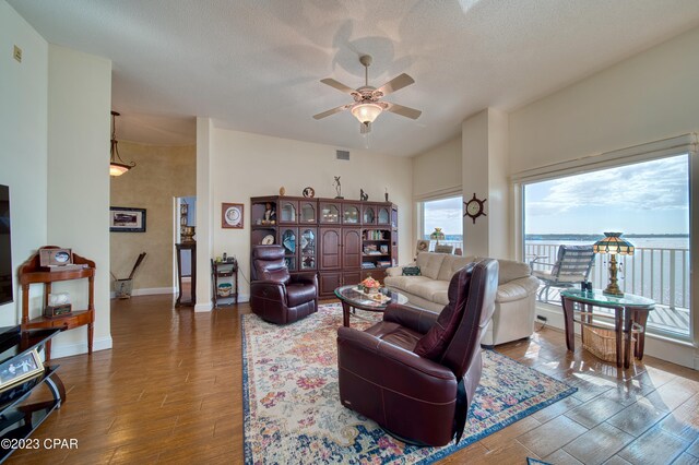 living room with ceiling fan, a water view, wood-type flooring, and a textured ceiling