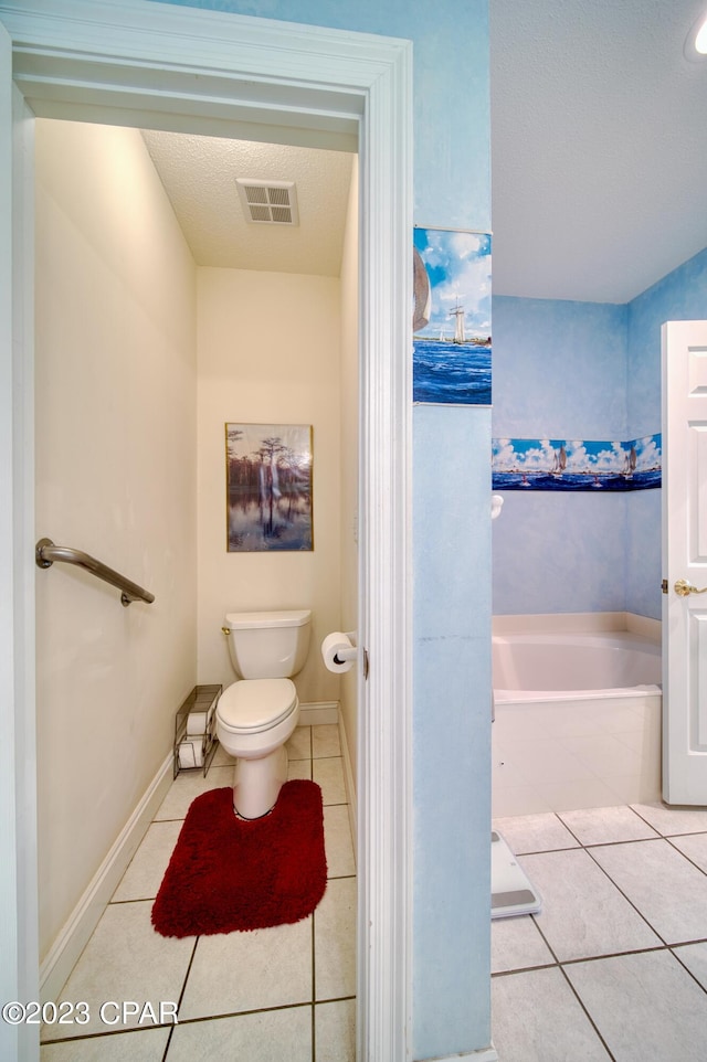 bathroom featuring tile patterned flooring, toilet, a tub to relax in, and a textured ceiling