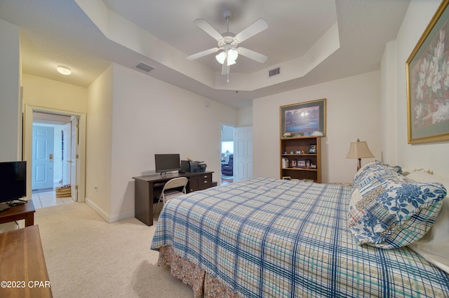 bedroom featuring ceiling fan, light colored carpet, and a tray ceiling