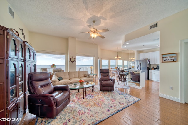 living room featuring ceiling fan with notable chandelier, light wood-type flooring, and a textured ceiling