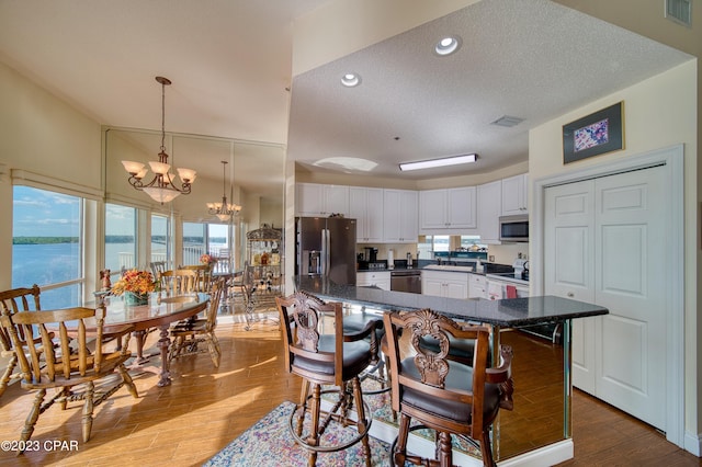 kitchen featuring white cabinets, a water view, a textured ceiling, stainless steel appliances, and a chandelier