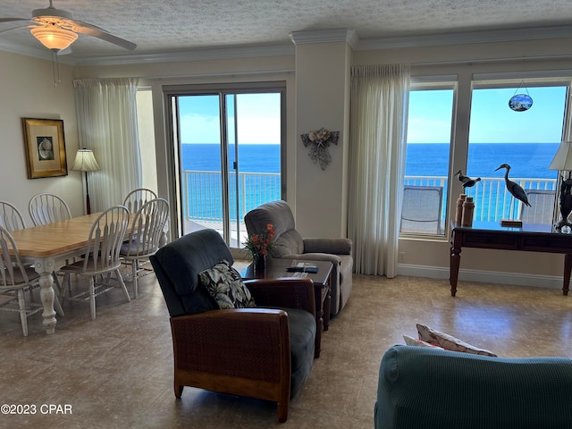 living room featuring a water view, ornamental molding, ceiling fan, and a textured ceiling