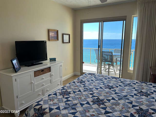 bedroom featuring a water view, a textured ceiling, access to outside, and multiple windows