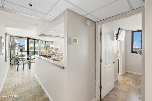 hall featuring sink, expansive windows, light tile patterned flooring, and a paneled ceiling