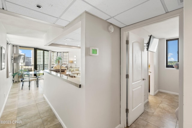 hall with light tile patterned flooring, a drop ceiling, and baseboards