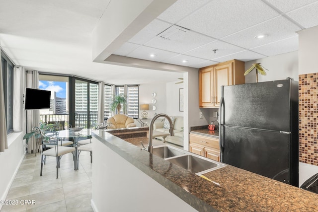 kitchen with light tile patterned floors, a paneled ceiling, dark countertops, freestanding refrigerator, and a sink