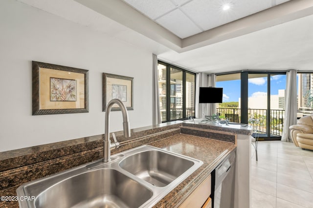 kitchen featuring light tile patterned floors, dark countertops, open floor plan, a sink, and stainless steel dishwasher