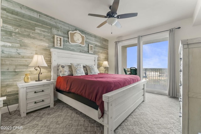 bedroom with wooden walls, light carpet, a ceiling fan, baseboards, and access to exterior