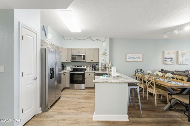 kitchen with sink, light hardwood / wood-style flooring, a textured ceiling, appliances with stainless steel finishes, and kitchen peninsula