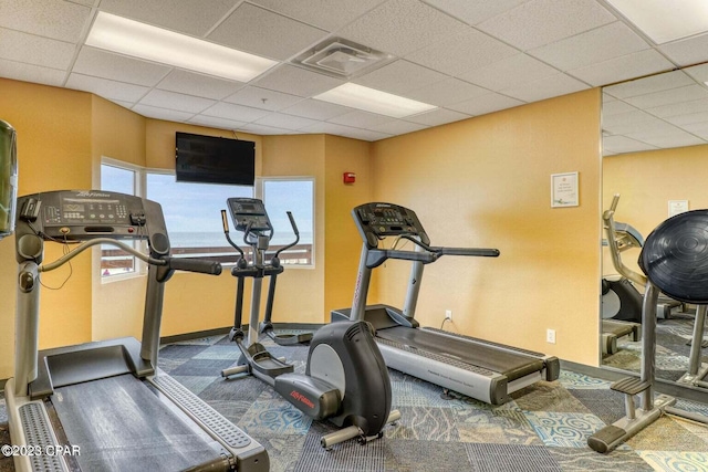 exercise area with dark carpet and a paneled ceiling