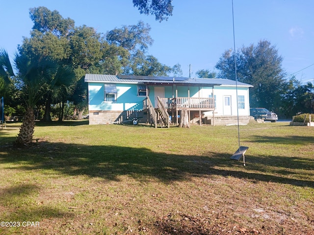 rear view of property featuring a lawn, solar panels, and a deck