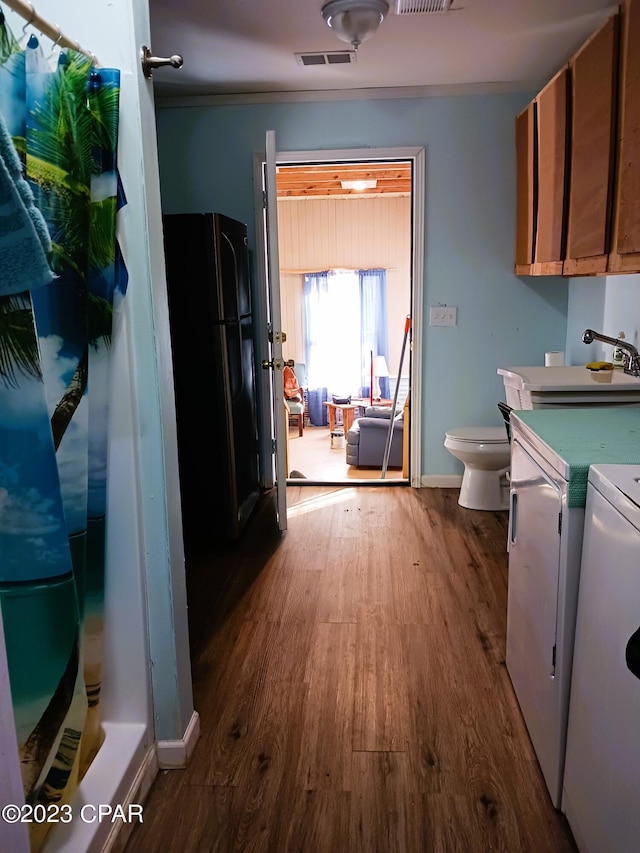 kitchen featuring washing machine and dryer, black fridge, and dark hardwood / wood-style flooring