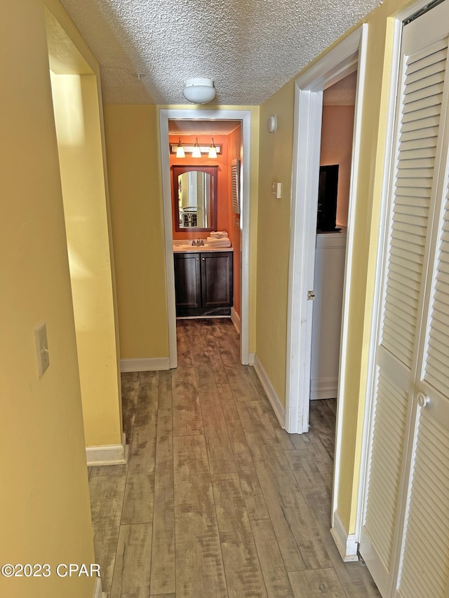 corridor featuring sink, a textured ceiling, and light wood-type flooring