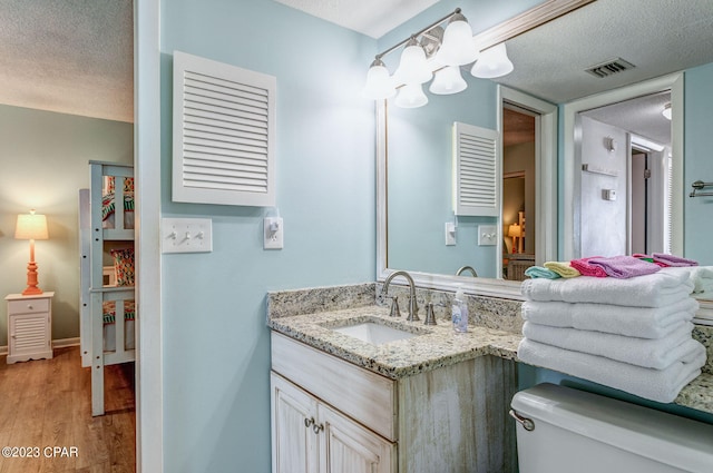 bathroom with toilet, vanity, a textured ceiling, and hardwood / wood-style flooring