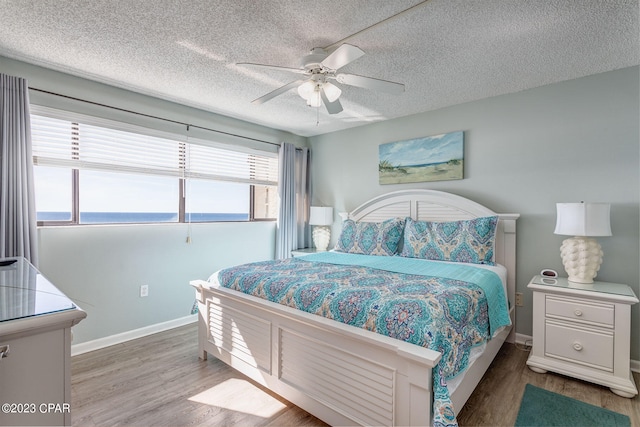 bedroom featuring wood-type flooring, a textured ceiling, a water view, and ceiling fan