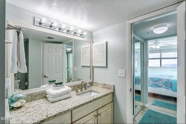 bathroom with vanity, a textured ceiling, ceiling fan, hardwood / wood-style flooring, and toilet