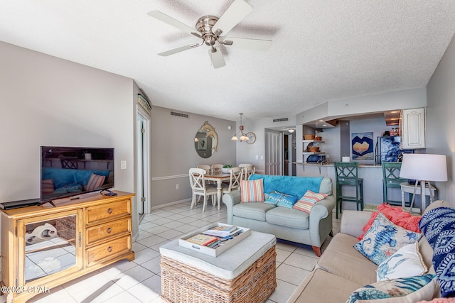 living room featuring ceiling fan with notable chandelier, light tile patterned floors, and a textured ceiling