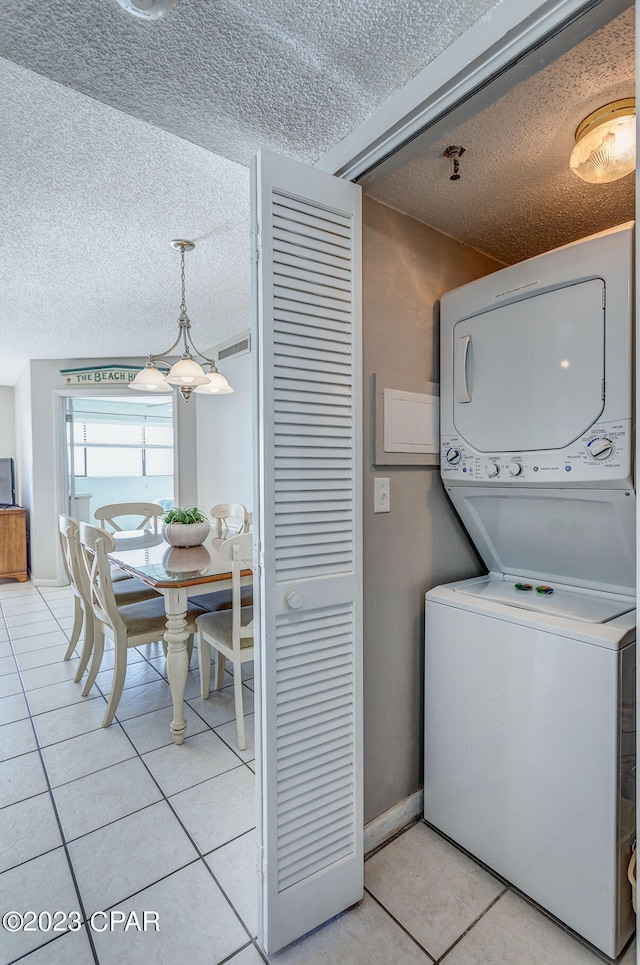 laundry room with a textured ceiling, light tile patterned flooring, and stacked washer / drying machine