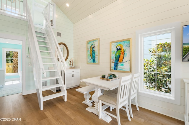 dining area with high vaulted ceiling, wood walls, and light hardwood / wood-style floors