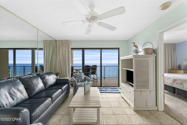 tiled living room with a water view, a textured ceiling, and ceiling fan