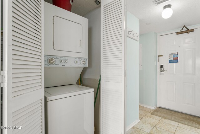 washroom with light tile patterned flooring, stacked washer and clothes dryer, and a textured ceiling