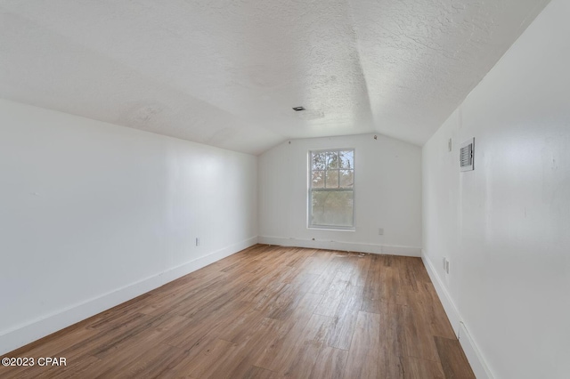 unfurnished room featuring lofted ceiling, hardwood / wood-style floors, and a textured ceiling