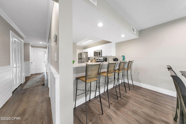 kitchen featuring kitchen peninsula, appliances with stainless steel finishes, dark hardwood / wood-style flooring, a breakfast bar, and white cabinets