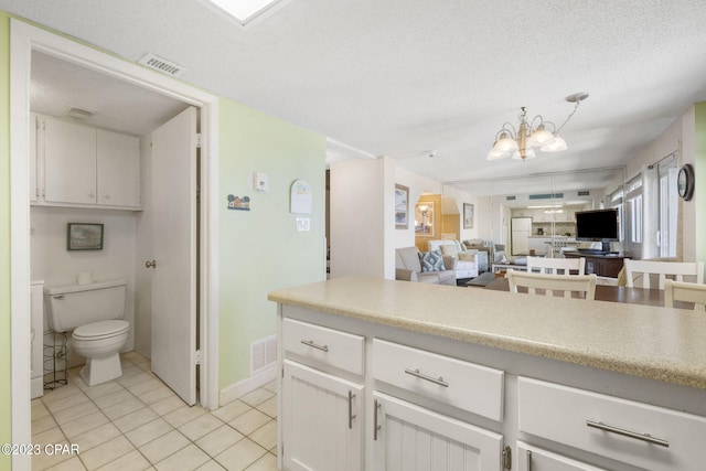 kitchen with decorative light fixtures, white cabinetry, light tile patterned floors, a textured ceiling, and an inviting chandelier