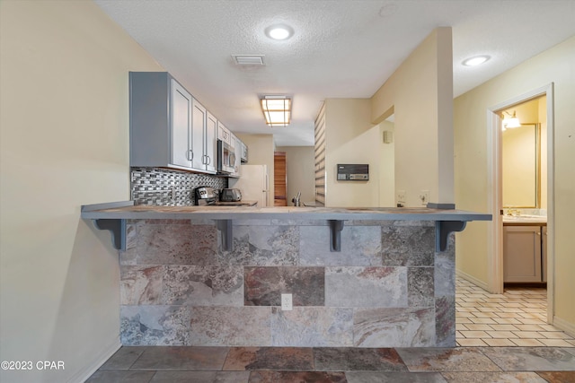 kitchen with white fridge, light tile patterned flooring, a textured ceiling, and kitchen peninsula