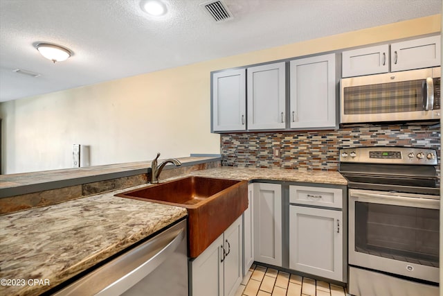 kitchen featuring light tile patterned flooring, appliances with stainless steel finishes, a textured ceiling, backsplash, and gray cabinetry