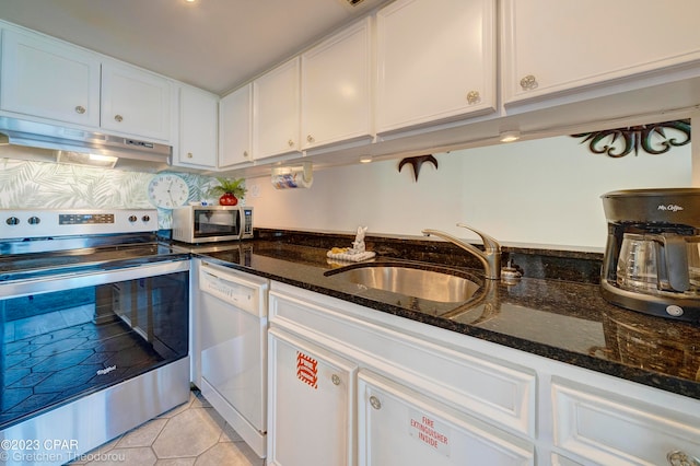 kitchen with appliances with stainless steel finishes, white cabinetry, dark stone countertops, light tile patterned flooring, and sink