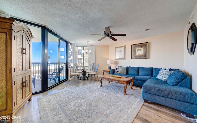 living room featuring ceiling fan with notable chandelier, light hardwood / wood-style floors, a textured ceiling, and a wall of windows