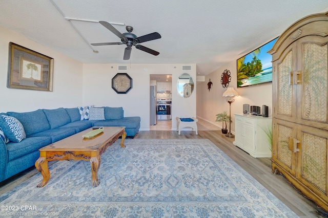 living room with ceiling fan, a textured ceiling, and light wood-type flooring