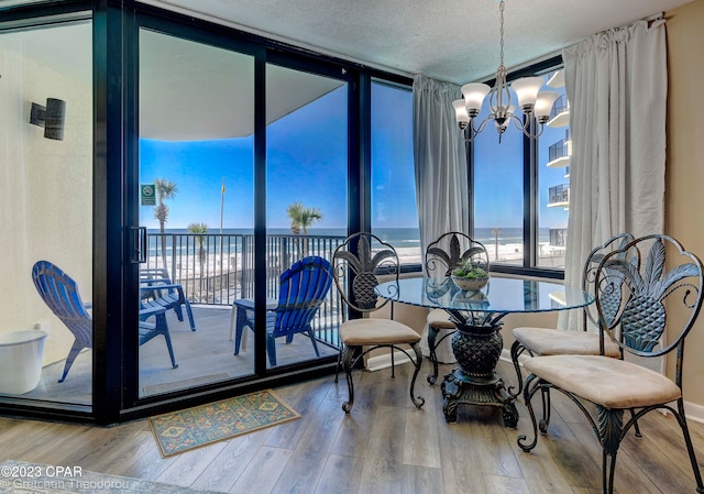 dining area with a textured ceiling, hardwood / wood-style floors, a wall of windows, a water view, and a notable chandelier